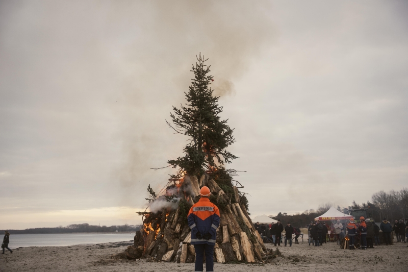 Ein großes Lagerfeuer am Strand zu Feuer und Meer mit Absicherung durch die Feuerwehr. 